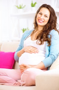 Pregnant smiling woman sitting on a sofa and caressing her belly