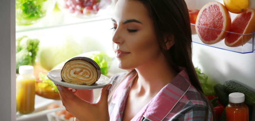 Young beautiful woman eating unhealthy food from the fridge at night
